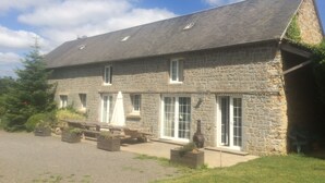 Un bâtiment en pierre doté d’un toit en pente, de nombreuses fenêtres et d’un espace extérieur aménagé pour s’asseoir.
