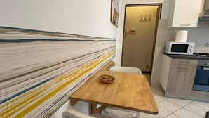 A small kitchen with a wooden table and white chairs, a microwave, and a door with a sign.