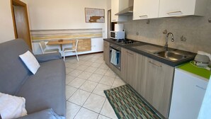 A compact kitchenette with a stove, sink, and microwave. There is a small dining area with a table and chairs.