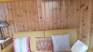 Un sofá con cojines estampados, un panel de pared de madera y una estantería con objetos decorativos.