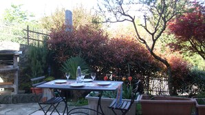 Un área de comedor al aire libre con una mesa preparada para dos personas, rodeada de plantas en macetas y un muro de piedra.