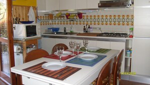 Una cocina con armarios blancos, un microondas, una cocina a gas y una mesa de comedor con platos y vasos.