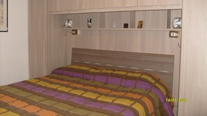 Un dormitorio con cama, cabecero y estante con diversos objetos.