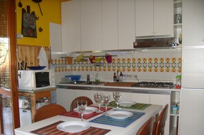 A kitchen with white cabinets, a microwave, a gas stove, and a dining table set with plates and glasses.