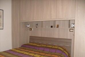 A bedroom with a bed, a headboard, and a shelf with various items.