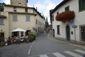 A narrow street lined with buildings, some with outdoor seating and flower boxes. - "TERRACE BELL" (PANZANO IN CHIANTI)
