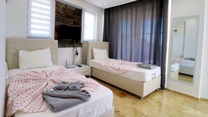 Ett modernt sovrum med två sängar, en eldstad i sten, en platt-TV och en stor spegel.