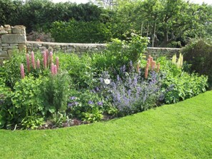Un jardin avec un mur en pierre, diverses plantes à fleurs et une pelouse bien entretenue.