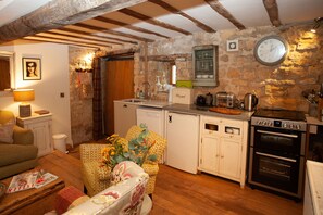 Cozy living space with a sofa, armchair, and wooden coffee table, featuring a kitchen area with sink, toaster, and refrigerator.