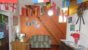 A living room with a sofa, a wooden desk, and a staircase. Flags are hanging from the ceiling.