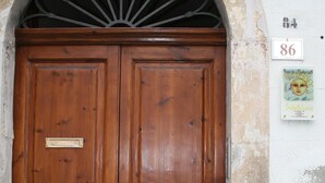 A wooden double door with a metal architrave, a plaque, and a sign with the number 86 on a white wall.