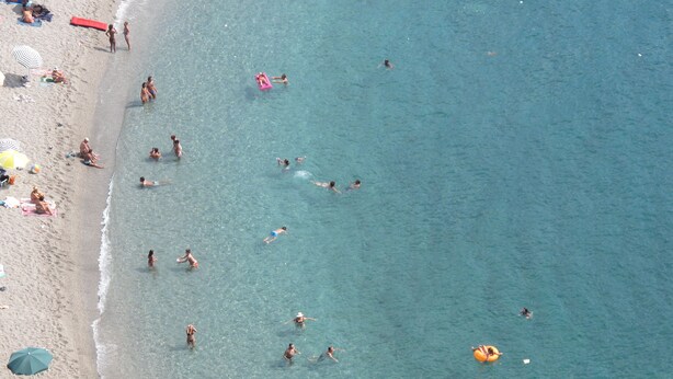 A beach with clear water, people swimming and sunbathing.