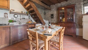 A rustic kitchen with wooden beams, a stone wall, and a wooden cabinet with glass doors. - Mimmo Holiday House Florence (San Godenzo, Firenze)