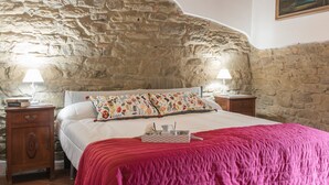 A bedroom with a stone wall headboard, a bed with a floral pillow, two bedside tables with lamps, and a painting on the wall. - Mimmo Holiday House Florence (San Godenzo, Firenze)