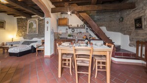 A rustic kitchen with a stone wall, wooden beams, and a dining table set for four. - Mimmo Holiday House Florence (San Godenzo, Firenze)