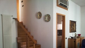 Una escalera conduce a un segundo piso, una cocina y un comedor con una silla azul.
