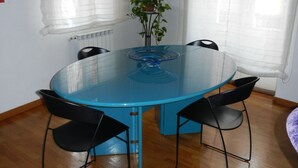 Una mesa redonda de vidrio con cuatro sillas negras, una planta en maceta y cortinas blancas.
