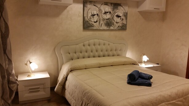 Un lit bien fait, avec une tête de lit et des oreillers de couleur beige, deux lampes de chevet et un tableau au-dessus du lit.