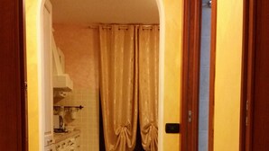 Un couloir doté d’un sol carrelé, d’une porte en arc de cercle et d’un coin cuisine avec des placards et un plan de travail.