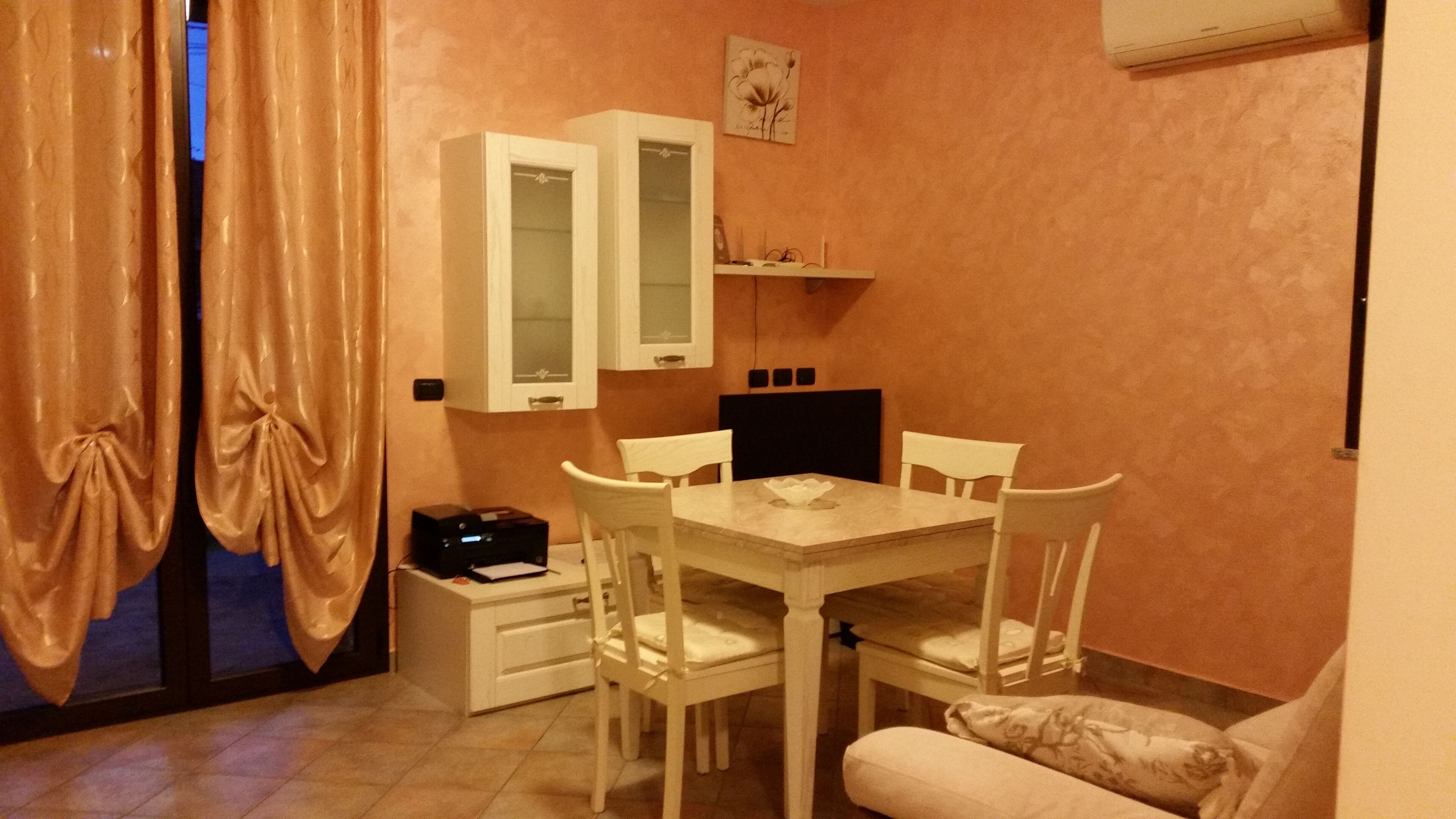 Una habitación pequeña y acogedora con una mesa de comedor y sillas, un aparador con puertas de cristal, una cama y un televisor.