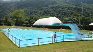 Ein Schwimmbecken mit einer weißen Kuppelkonstruktion, umgeben von einer Rasenfläche und einer Bergkulisse.