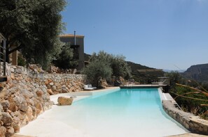 A swimming pool with a stone wall and a building with a tiled roof. - Houses with swimming pool with magnificent view to the sunset (Alyki)