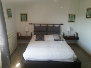 A neatly made bed with a white comforter and two pillows, one with an Eiffel Tower design. There are two bedside tables with lamps and books, and a radiator on the left.