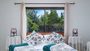 Camera d'albergo con un letto, biancheria da letto a fiori, asciugamani, vista su alberi e due lampade sui comodini.