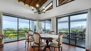 Un'area pranzo con un tavolo grande e sei sedie, ampie finestre con vista sul verde e un lampadario.