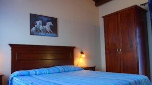 Une chambre à coucher avec un lit en bois, une couvre-lit à rayures bleues, une table de chevet avec une lampe et une armoire.