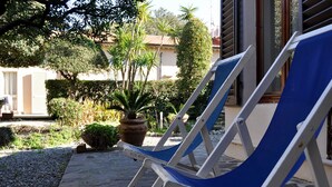 Two blue lounge chairs in a garden area with a stone pathway, potted plants, and a building in the background. - Beautiful house in Villa Liberty  (Marina di pisa)