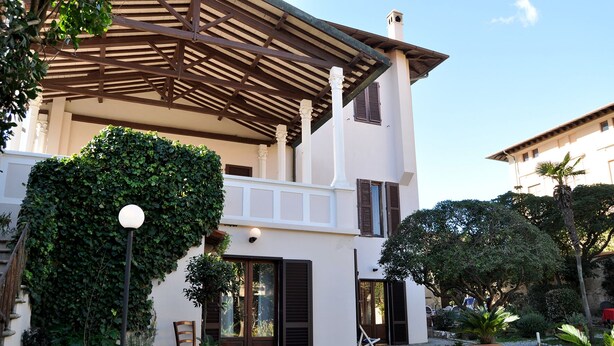 A two-story building with a covered patio area, potted plants, and a chair. - Beautiful house in Villa Liberty  (Marina di pisa)