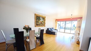 A spacious living area with a dining table, chairs, a sofa, and a large window with a view. - Villa Luz: between Serra and the Sea - Free Wifi (Santa Cruz)