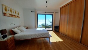 A bedroom with a bed, bedside table, lamp, and a painting on the wall. - Villa Luz: between Serra and the Sea - Free Wifi (Santa Cruz)