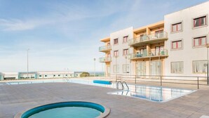 A rooftop swimming pool area with a large pool and a smaller circular pool, surrounded by a building with balconies.