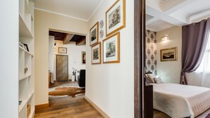 A bedroom with a bed, a wardrobe, and a desk. There are framed pictures on the wall and a window with curtains.