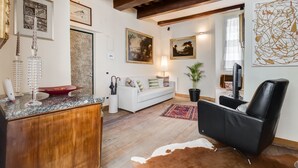 A modern living room with a wooden ceiling, a white sofa, a black leather chair, a TV, and various wall art.