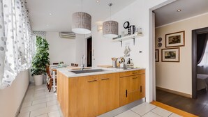 A modern kitchen with a wooden island, pendant lights, and a potted plant.