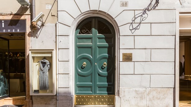 A green double door with a brass doorknob, a small display window to the left, and a white brick wall.
