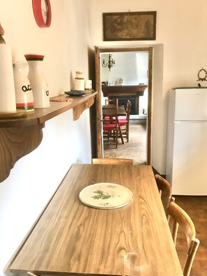 A wooden dining table with a plate, chairs, a shelf with bottles, and a refrigerator in a kitchen. - Bargi House (Perugia)