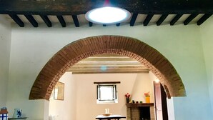 An interior with a brick archway, wooden beams, a table with benches, and a hanging light fixture. - Bargi House (Perugia)