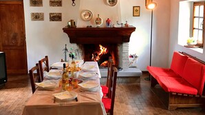 A dining area with a fireplace, wooden beams, and a red sofa. - Bargi House (Perugia)