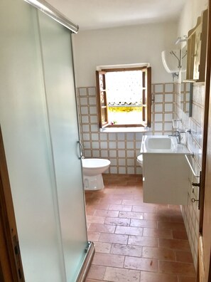 A bathroom with a toilet, a sink, and a window with a view of a garden. - Bargi House (Perugia)