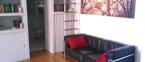 Una habitació amb un sofà de pell negra, una biblioteca i vista a una paret de maó.