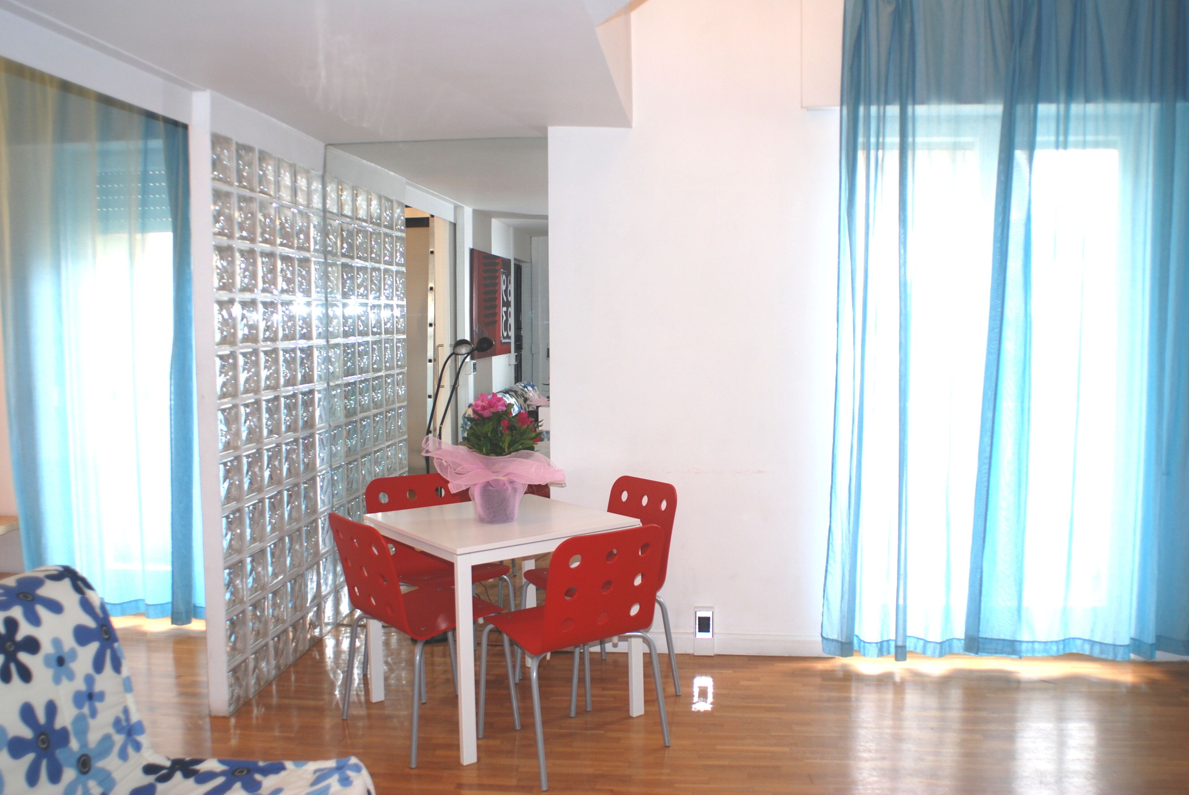 Uma área de refeições com uma mesa branca, cadeiras vermelhas e um arranjo floral rosa.