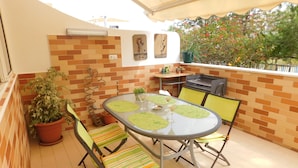 Eine Terrasse mit einem runden Tisch, Stühlen, einem Grill und Topfpflanzen.