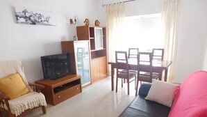 Ein Wohnzimmer mit Sofa, Fernseher, Holzschrank und Essbereich.
