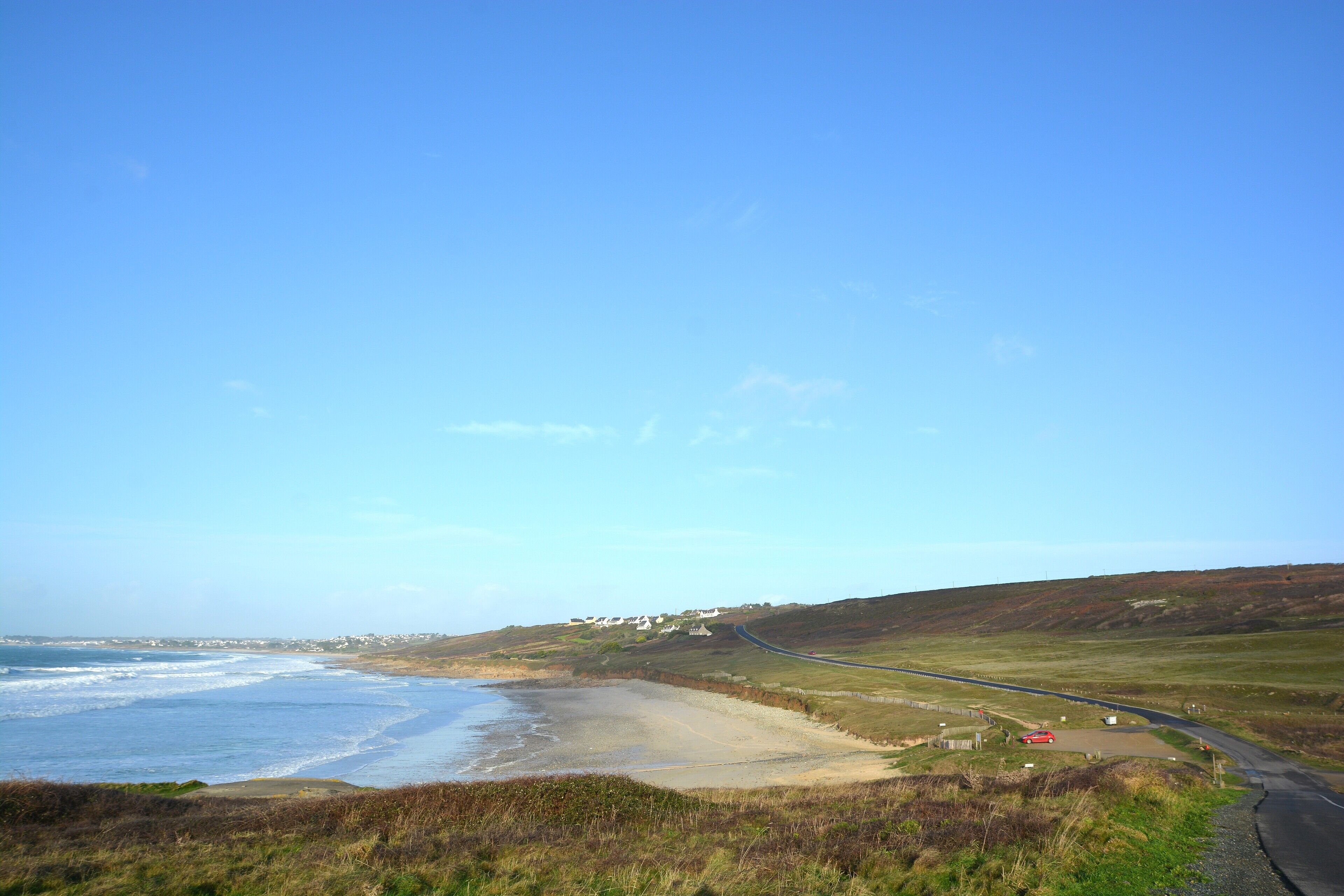 Una carretera costera con una playa y casas a lo lejos.
