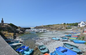 Un paysage côtier avec des bateaux amarrés le long d’une rive rocheuse, un phare et un mur de pierre.