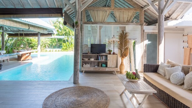 Un espace extérieur abrité comprenant une piscine, un canapé et un téléviseur posé sur un meuble en bois.